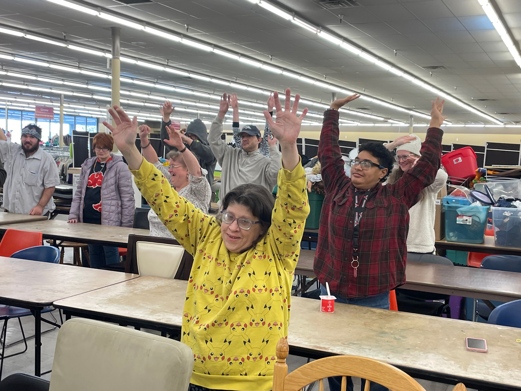 A group of adults with disabilites raising their arms in the air inside of a charity thrift shop