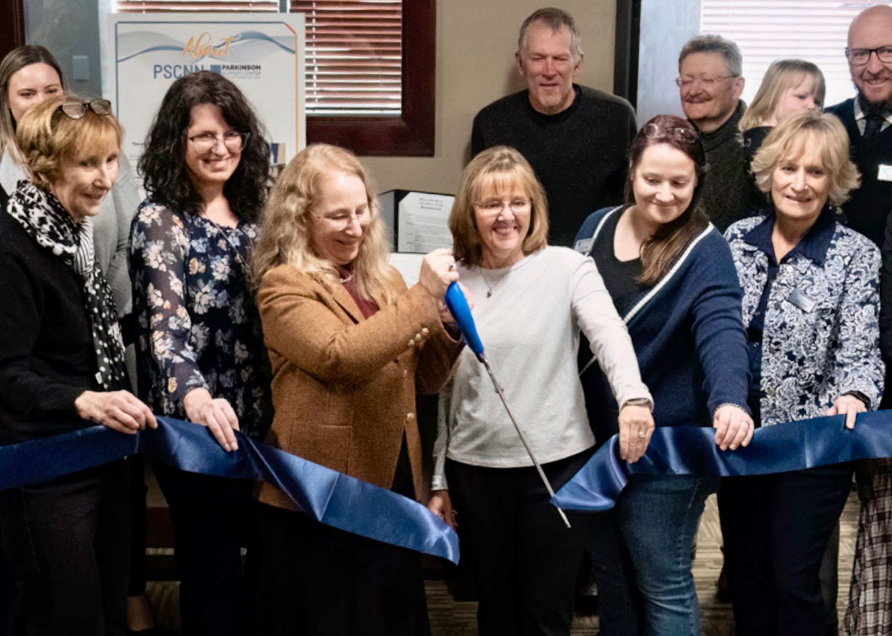 A group of board members from Parkinson Support Center of Northern Nevada cutting a blue ribbon with a large pair of scissors